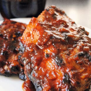 Two half racks of baby back ribs with barbecue sauce, with bottle of root beer in background.