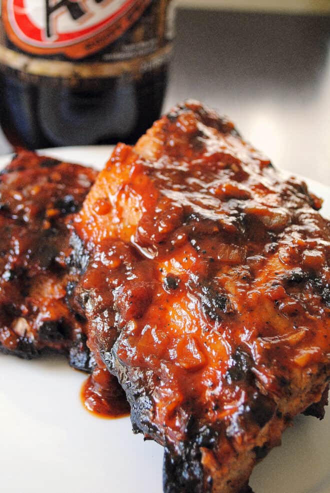 Two half racks of baby back ribs with barbecue sauce, with bottle of root beer in background.