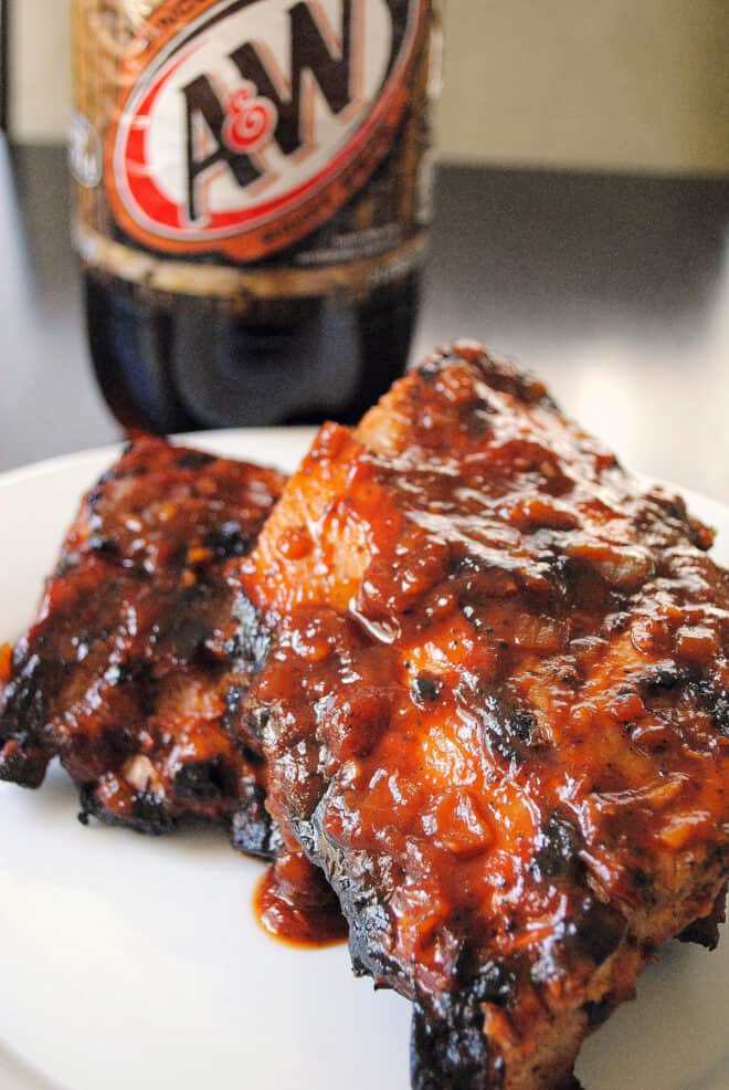 Two half racks of baby back ribs with barbecue sauce, with bottle of root beer in background.