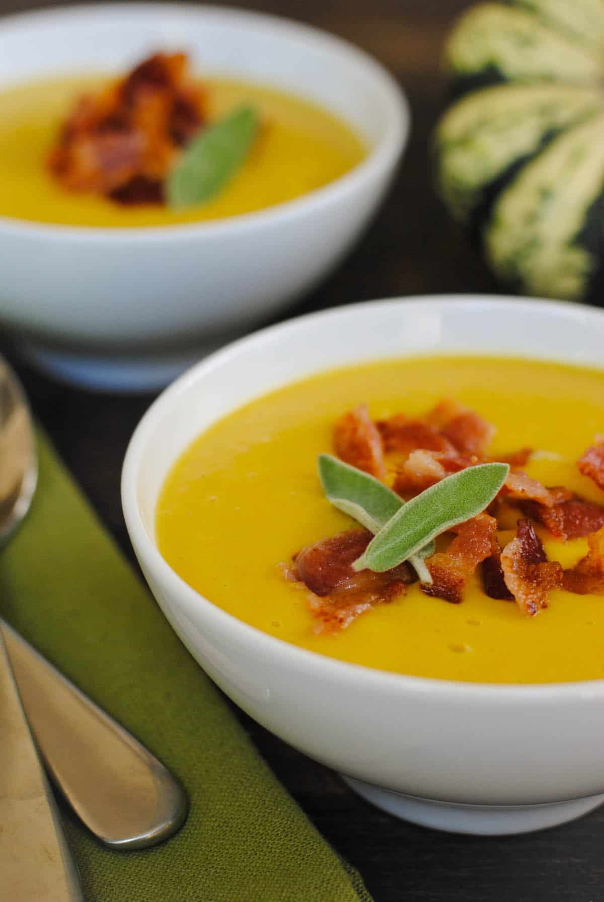 Two bowls of squash soup, topped with bacon and sage leaves.