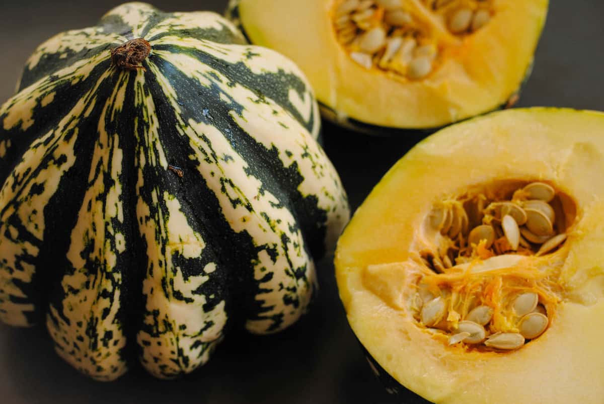 Two dumpling squashes, one whole and one cut in half, exposing seeds.