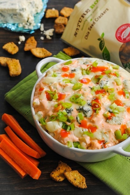 Creamy spicy dip with chicken in white round baking dish with crackers and veggies for dipping.