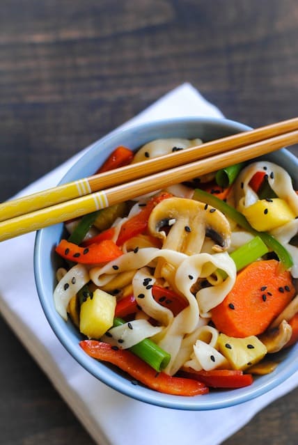 Closeup on blue bowl filled with sweet and sour vegetable stir fry, with chopsticks resting on top of bowl.