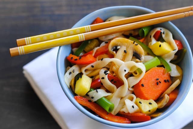 Blue bowl filled with Sweet and Sour Vegetable Stir Fry with yellow decorated chopsticks resting on top.