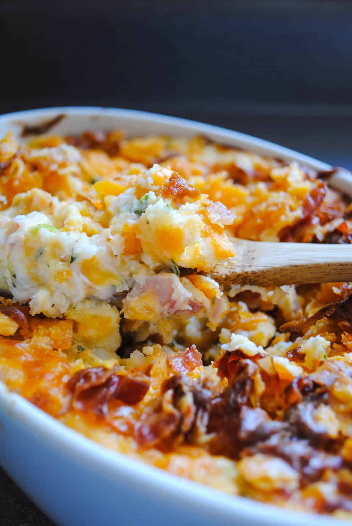 Closeup of loaded mashed potato bake casserole with wooden spoon in it.