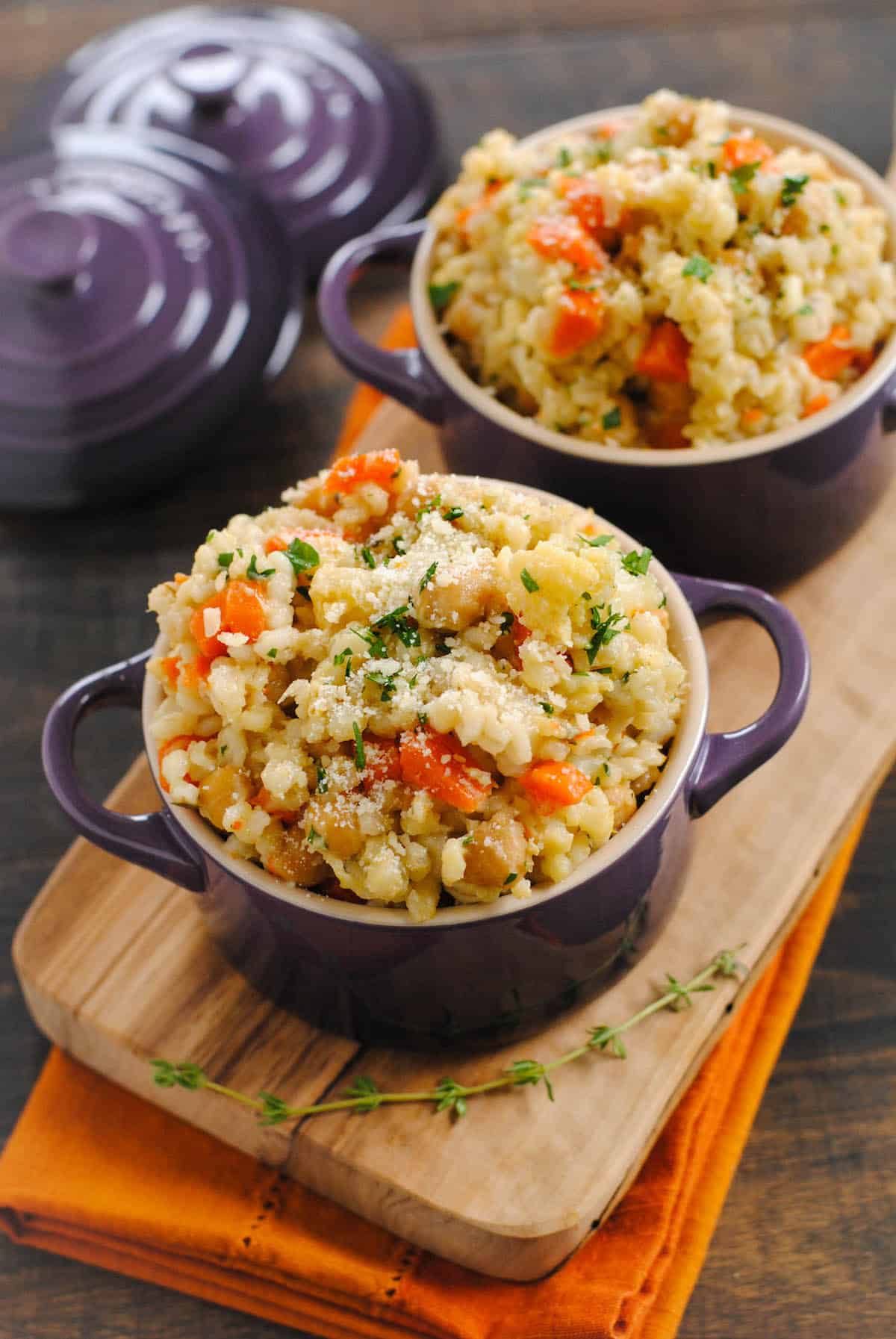 Slow cooker barley and vegetable side dish in small purple pots on wooden cutting board.