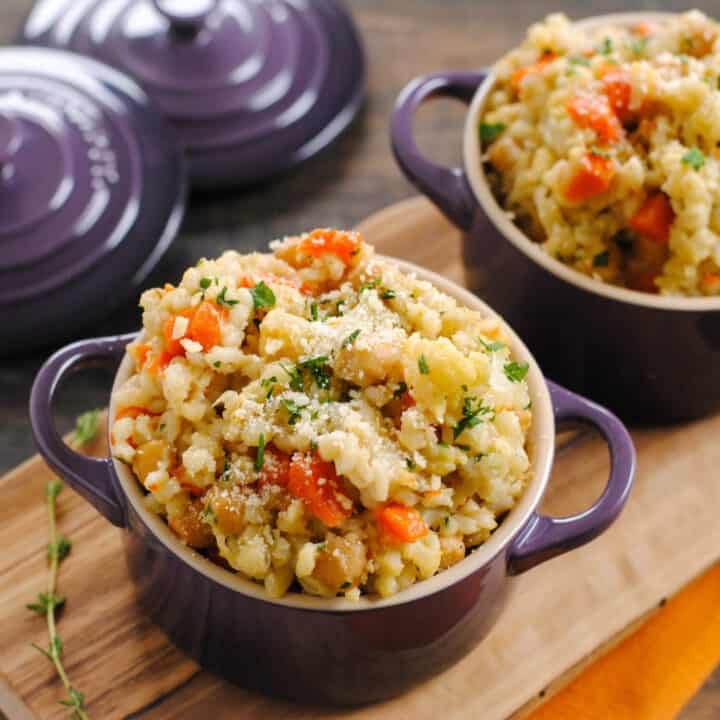 Barley and vegetable side dish in small purple pots on wooden cutting board.