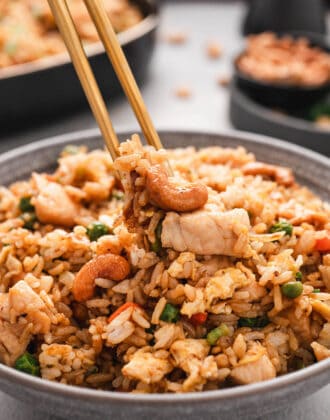 A grey bowl filled with easy chicken fried rice, with a pair of chopsticks lifting out a bite.