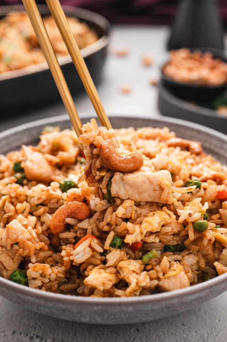 A grey bowl filled with easy chicken fried rice, with a pair of chopsticks lifting out a bite.