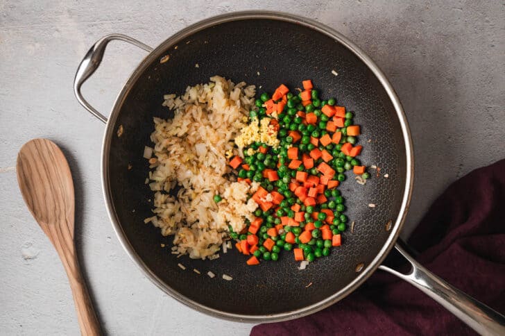 A dark nonstick skillet filled with sauteed onions, peas and carrots.