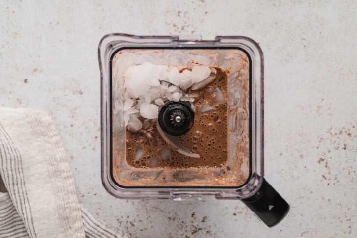 A square blender pitcher filled with a blended brown mixture and ice.