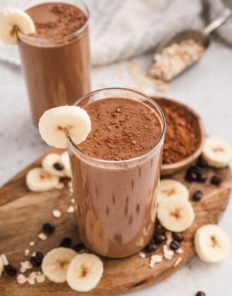 Two glasses of a coffee breakfast smoothie recipe, garnished with cocoa powder and sliced bananas.