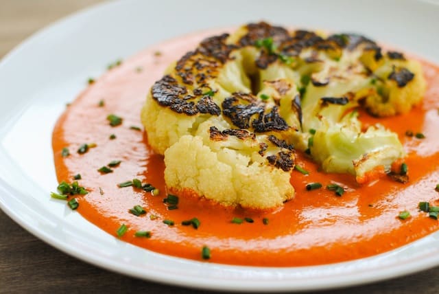 Seared Cauliflower Steaks with Red Pepper-Walnut Sauce - A Meatless Monday dish that still eats like a steak. Big slices of cauliflower are seared in a cast iron skillet then finished in the oven, for a crunchy golden brown crust on the outside. Served over a ladle of Spanish-inspired pureed red pepper and walnut sauce. | foxeslovelemons.com