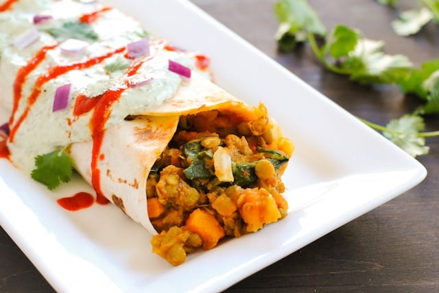 Rectangular white plate topped with burrito filled with spinach, sweet potatoes and lentils. Cilantro on table in background.