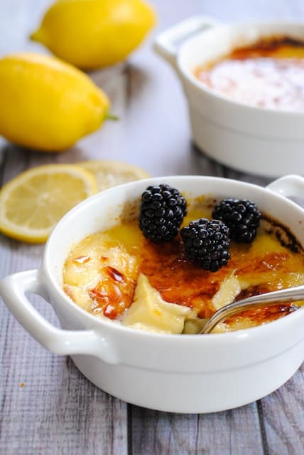 Torched custard in white dish topped with blackberries. Silver spoon dipped into custard.