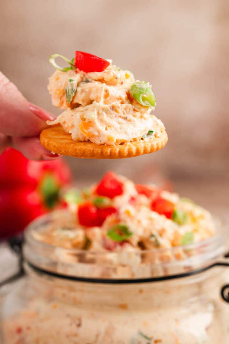 A hand holding a butter cracker topped with pimento cheese dip.