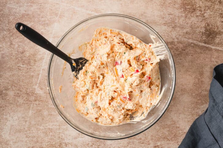 Homemade pimento cheese being stirred together in a glass bowl.