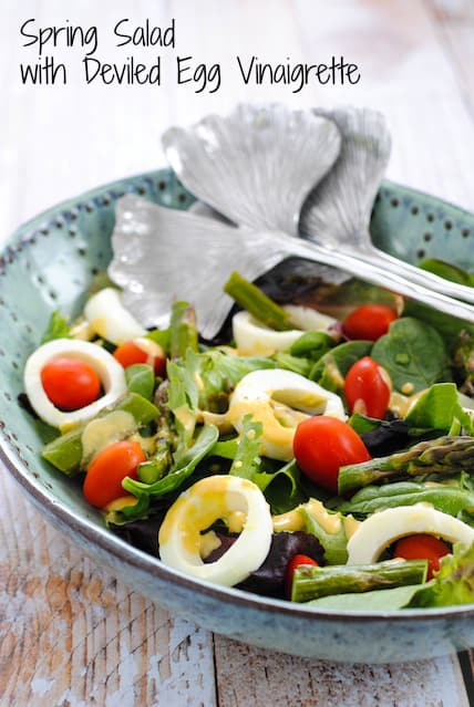 A large teal ceramic bowl filled with greens, hard boiled eggs, tomatoes and asparagus.