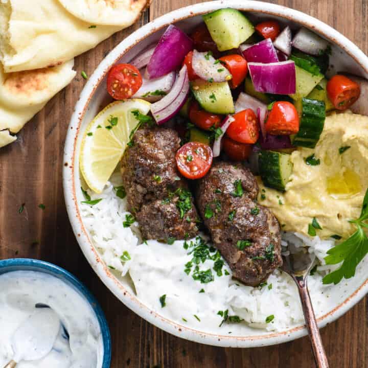 Bowl with kafta, hummus, yogurt sauce and a chopped vegetable salad on a wooden background.
