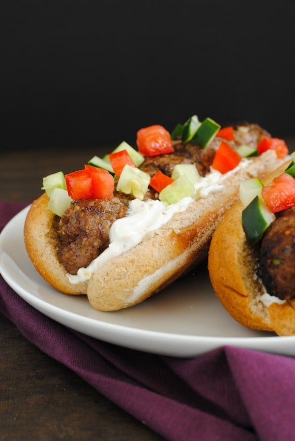 Hot dog buns filled with cooked ground beef logs, topped with yogurt, tomatoes and cucumber.