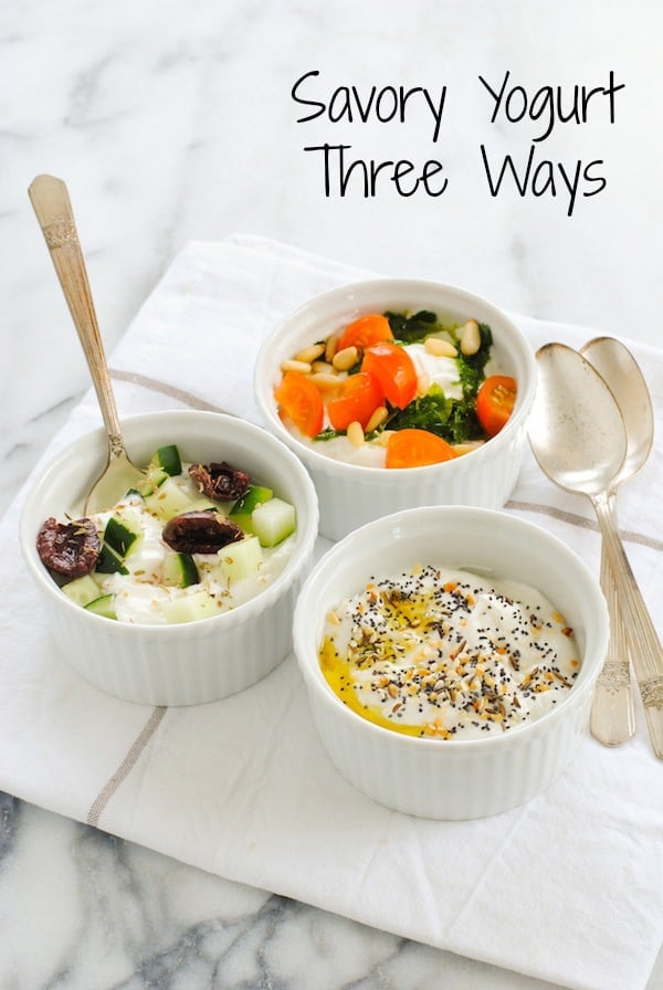 Three white ramekins of savory Greek yogurt recipes, including bowls topped with everything bagel seasoning, olives and cucumbers, and tomato, basil pesto and pine nuts.