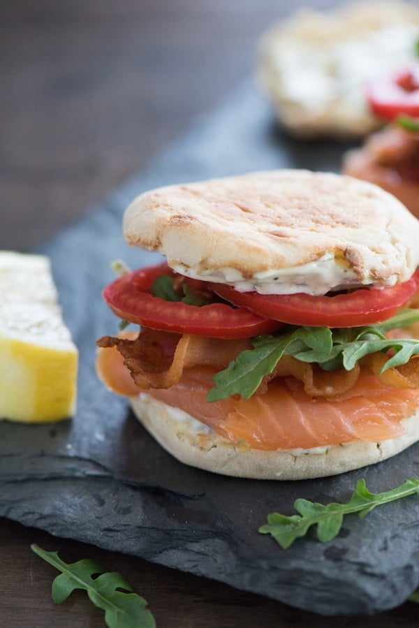 An english muffin filled with smoked fish, arugula and tomatoes on a slate board.