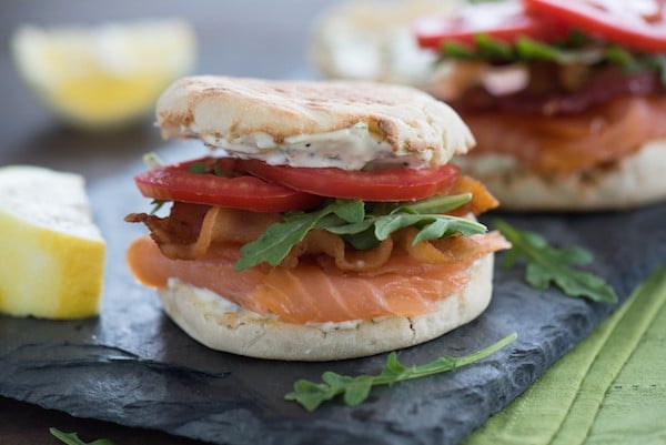 Smoked Salmon BLT with Lemon-Herb Mayonnaise - A fun twist on a classic sandwich that can be enjoyed for breakfast, brunch, lunch or dinner! | foxeslovelemons.com An english muffin filled with smoked fish, arugula and tomatoes on a slate board.