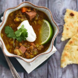 Lentil and sausage soup in rustic bowl with naan bread on side.