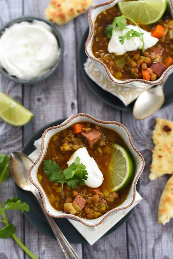 Overhead photo of two bowls of lentil soup, with naan bread, lime wedges and yogurt.