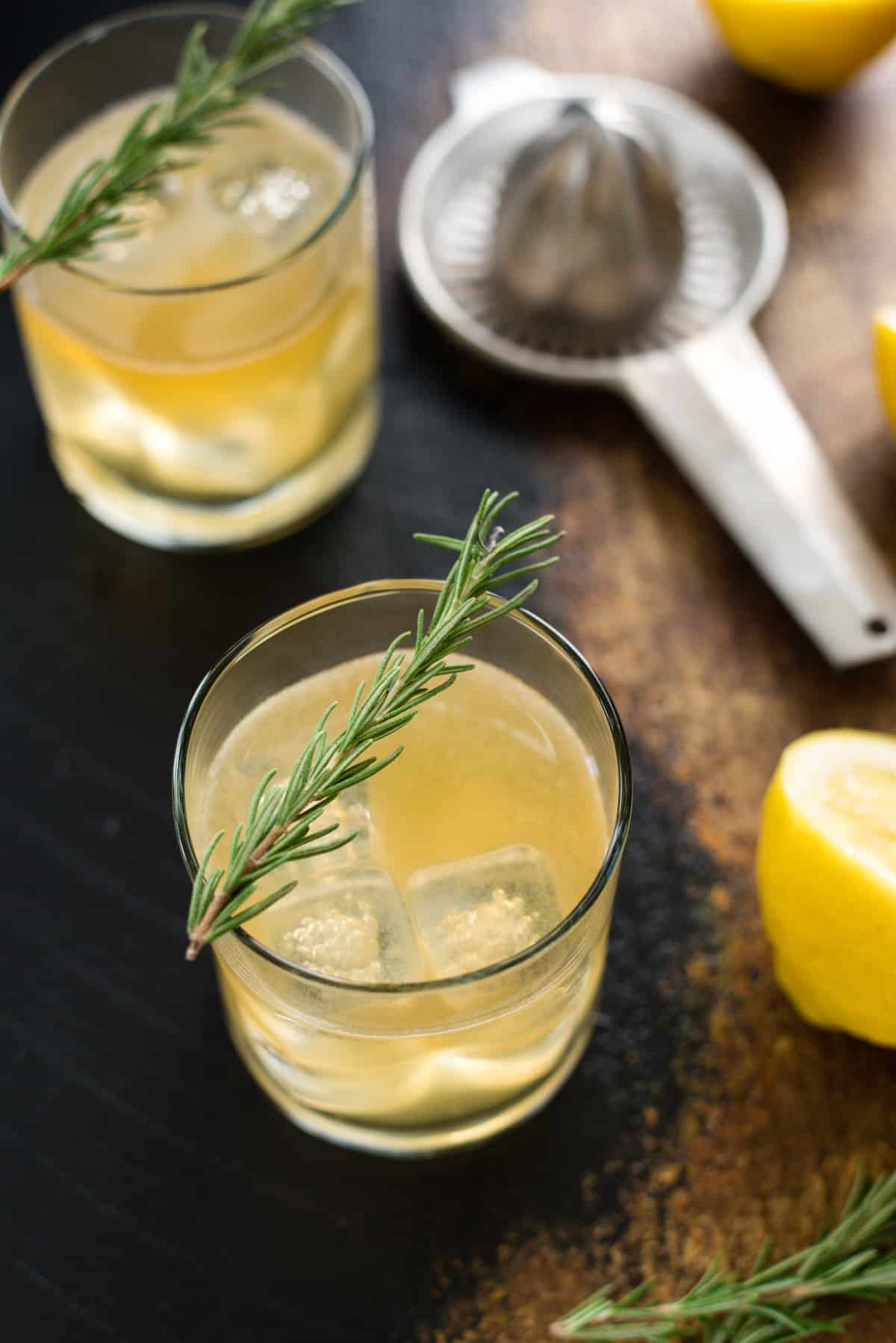 A glass filled with a bourbon lemon cocktail garnished with a rosemary sprig.