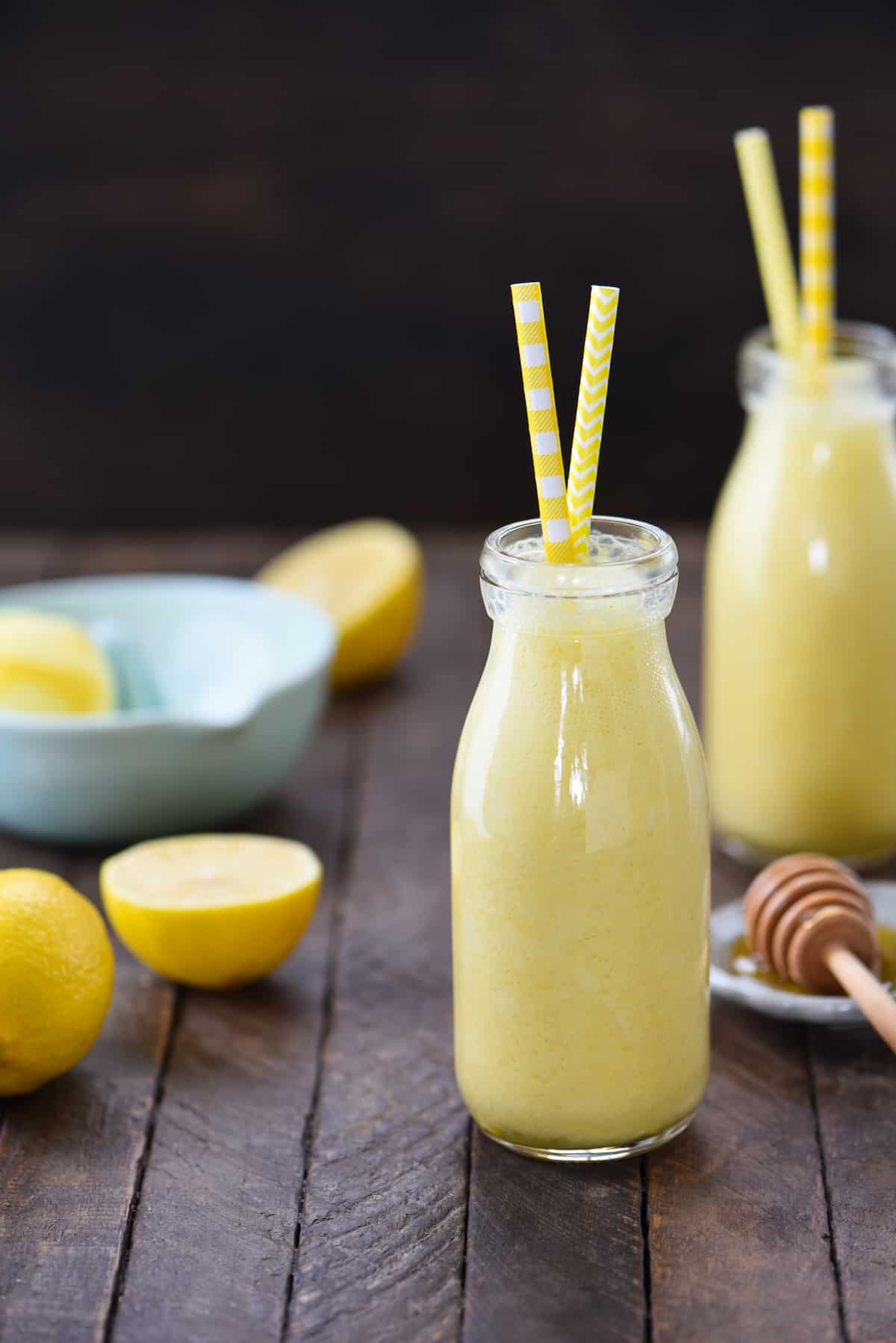 Two small glass bottles filled with lemon smoothie, with yellow straws sticking out of the bottles.