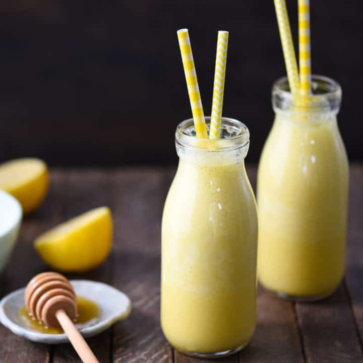 Two small glass bottles filled with lemon smoothie, with yellow straws sticking out of the bottles.