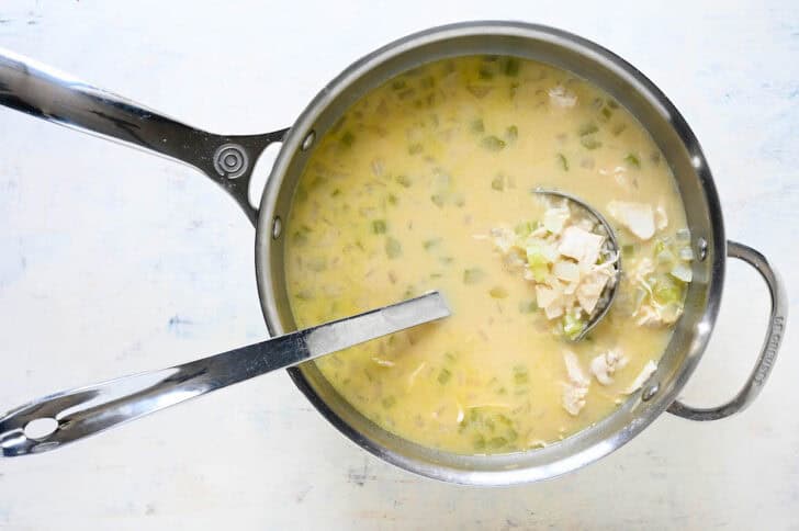 A stainless steel pot filled with a lemon chicken soup recipe with a ladle scooping some out.