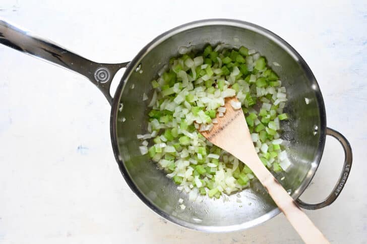 A stainless steel pot filled with chopped celery and onion being sauteed.