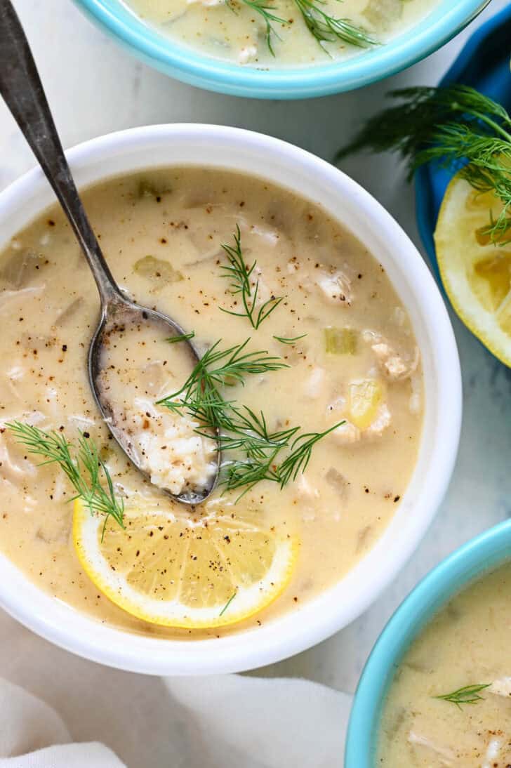 A white bowl filled with Greek lemon chicken soup garnished with fresh dill.