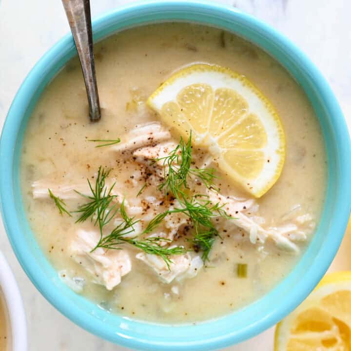 A teal bowl filled with lemon chicken soup garnished with dill.