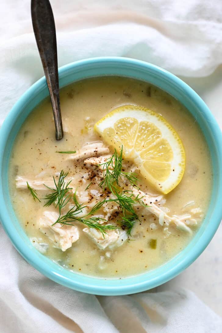 A teal bowl filled with lemon chicken soup garnished with dill.