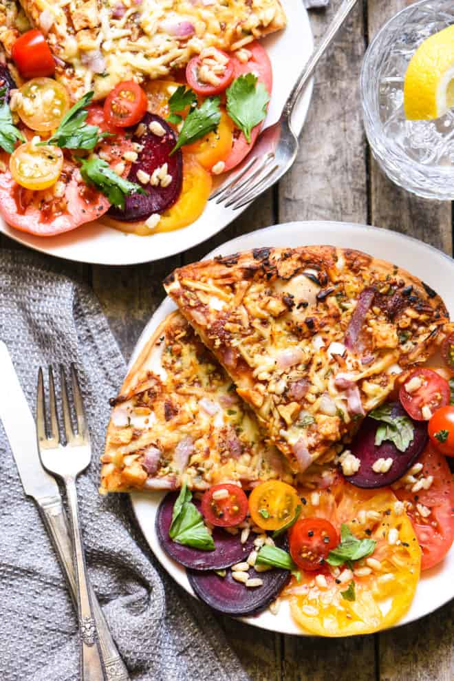 Two plates filled with pizza slices and tomato and beet salad. Forks alongside.