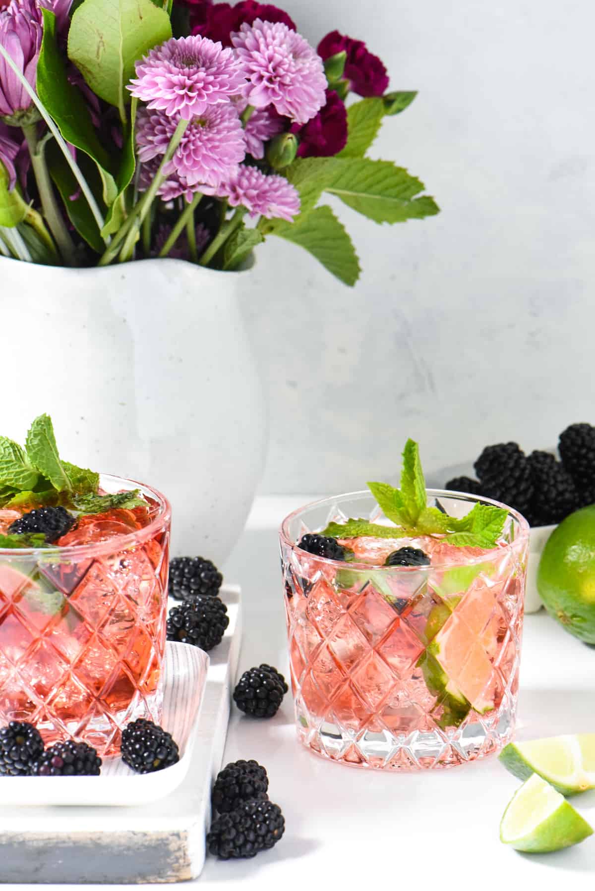 Two etched cocktail glasses filled with tequila mojjito and garnished with mint and blackberries.