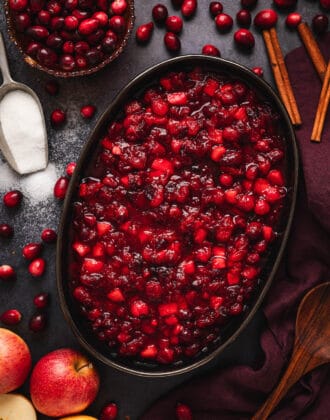 Homemade Cranberry Sauce in a black oval bowl, with the ingredients to make the sauce scattered around the scene.