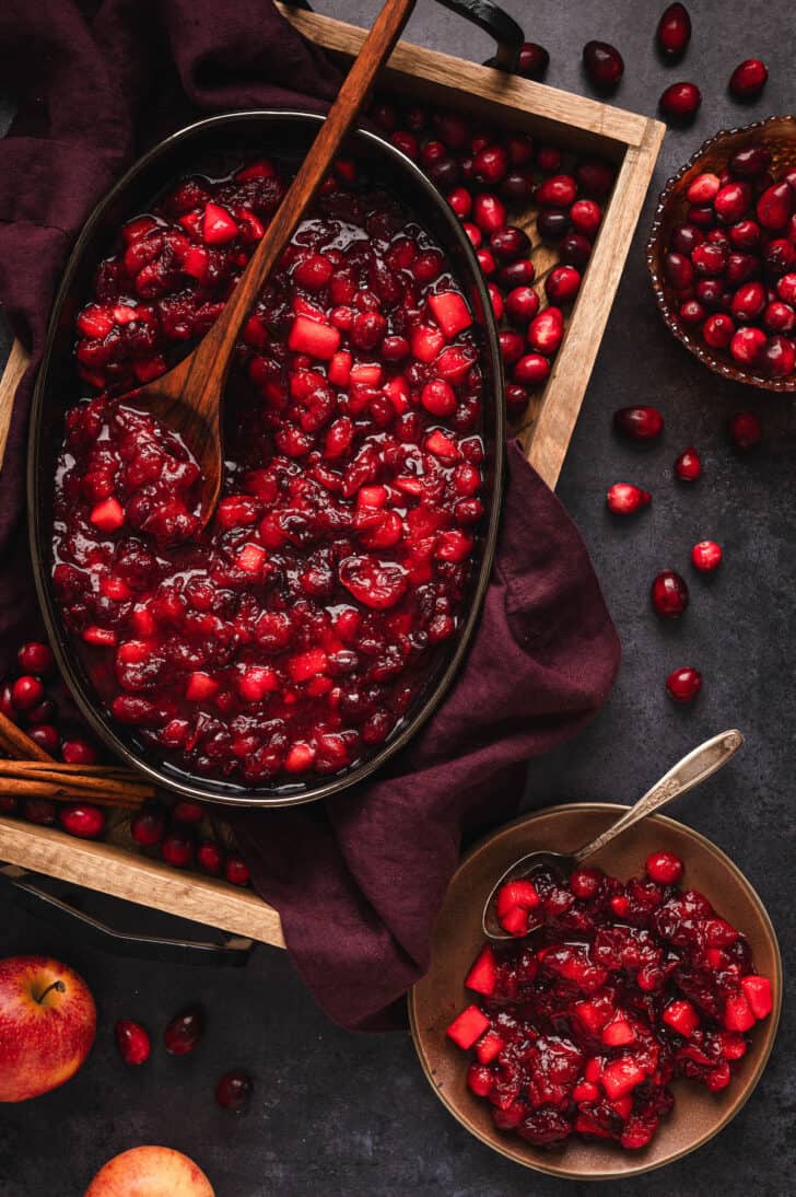 Whole berry cranberry sauce in a black serving dish, with a wooden spoon digging into it.