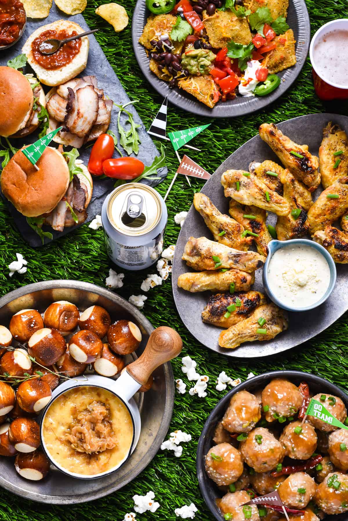 Astroturf topped with various types of tailgating food, including sliders, nachos, chicken wings cheese dip and meatballs.