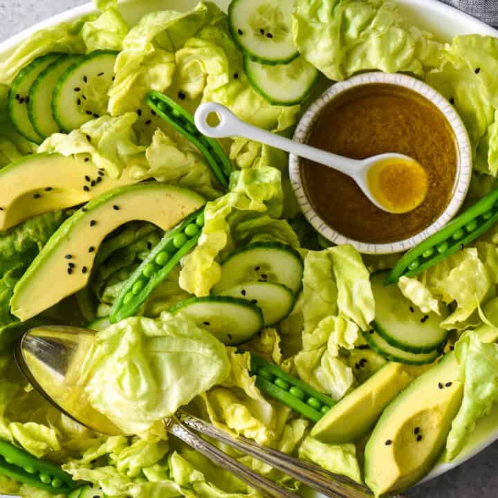 Large platter of all green salad ingredients with bowl of golden brown salad dressing.