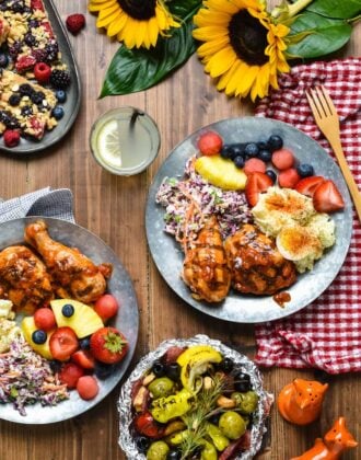 A wooden table topped with plates of barbecue party dishes.
