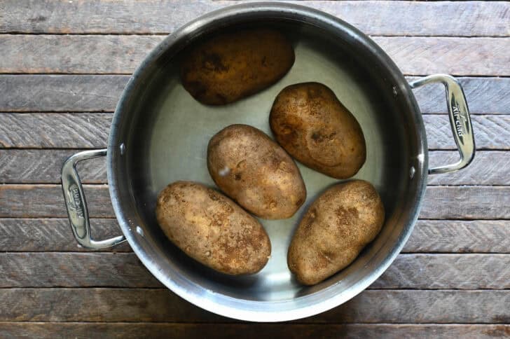 A stainless steel pot filled with 5 potatoes submerged in water.