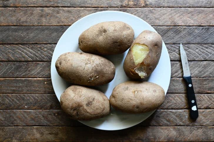 5 spuds on a white plate, with the skin being peeled off of one.