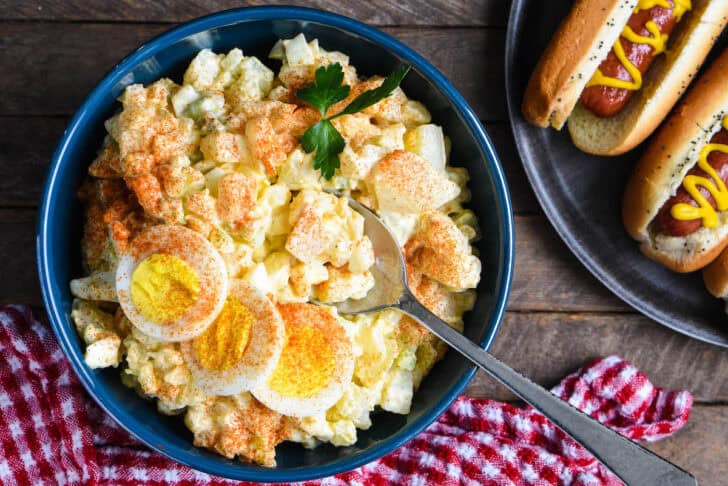 A blue bowl filled with a potato salad with egg recipe.