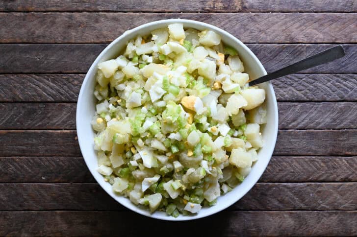 Chopped potatoes, celery, onion and eggs in a white bowl.