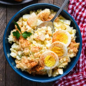 A blue bowl filled with potato salad with egg.