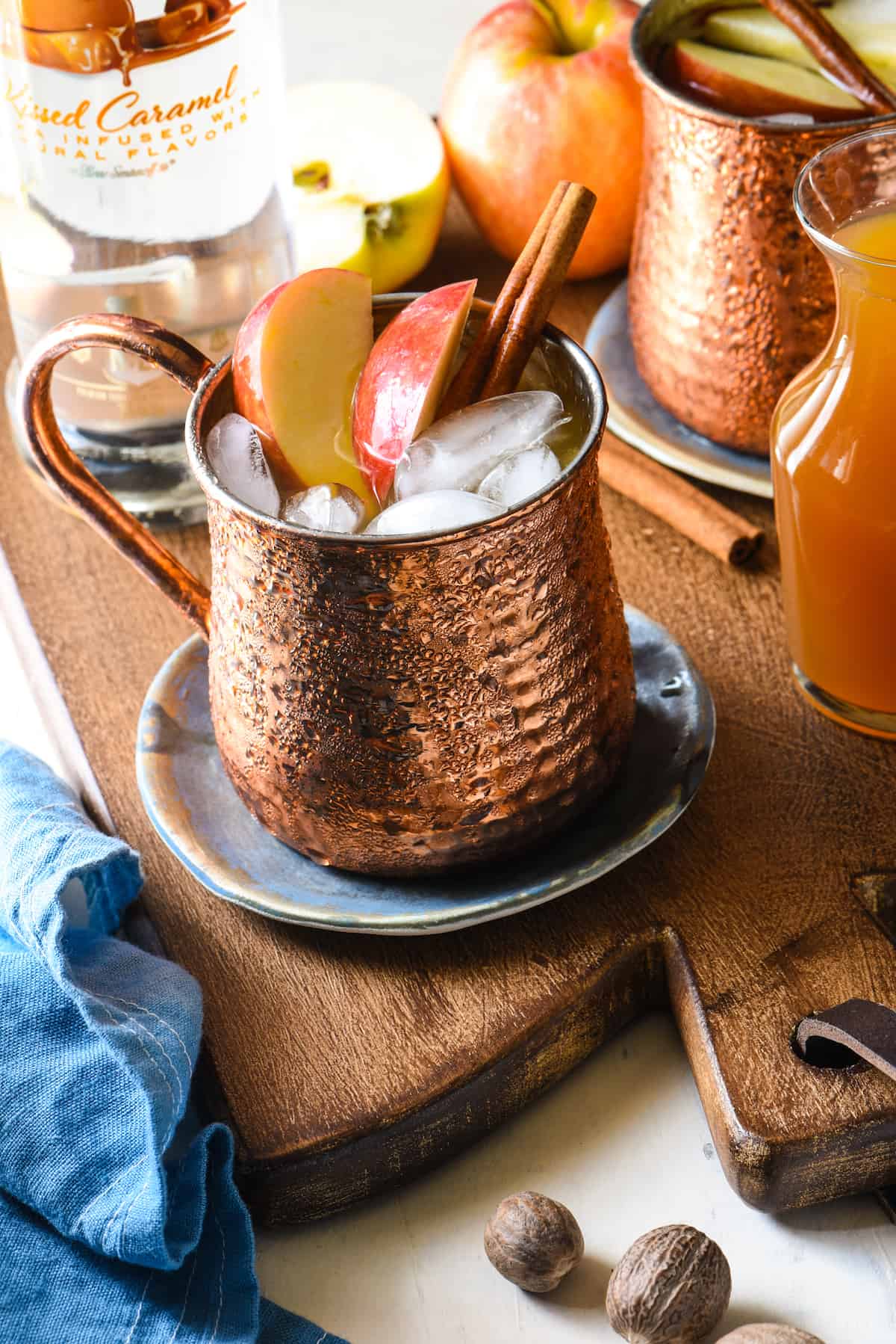 Copper Moscow mule mug filled with apple cider and vodka, garnished with fresh apple slices and cinnamon sticks.